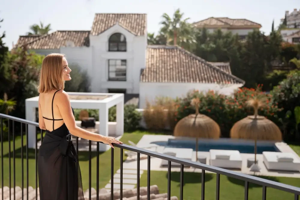 Una mujer sonriendo asomada en una baranda contemplando una finca de lujo